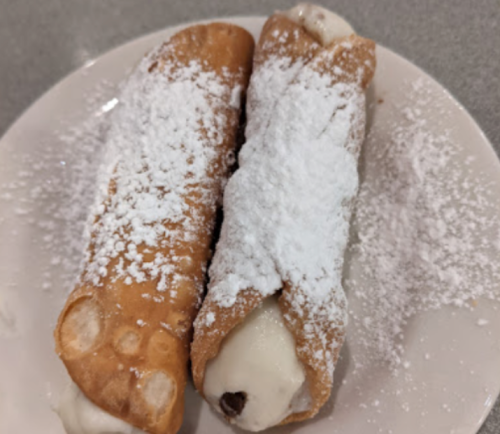 Two cannoli on a plate, filled with creamy filling and dusted with powdered sugar.