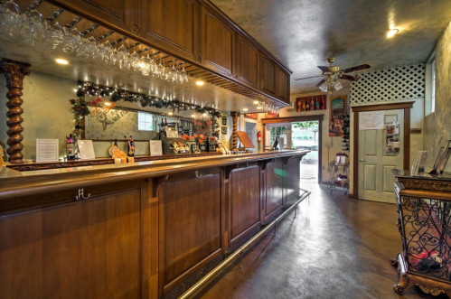 A wooden bar with glassware hanging above, decorated with lights and a cozy atmosphere, leading to an outdoor area.