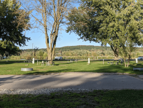 A serene park scene with picnic tables, trees, and a distant hillside under a clear blue sky.
