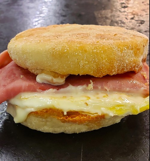 A close-up of a breakfast sandwich with a toasted English muffin, ham, egg, and creamy sauce.