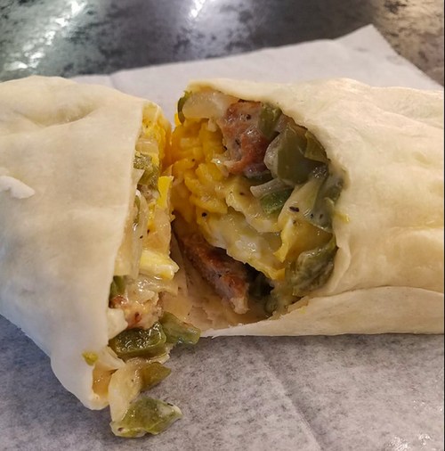 Close-up of a burrito cut in half, revealing a filling of rice, sausage, and green peppers wrapped in a soft tortilla.