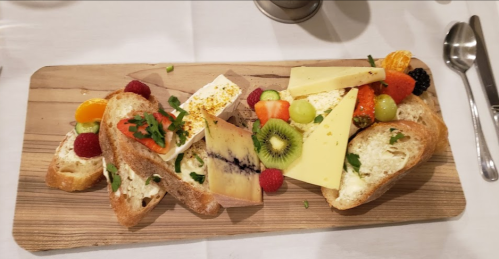 A wooden platter with assorted cheeses, fruits, and slices of bread, garnished with herbs.