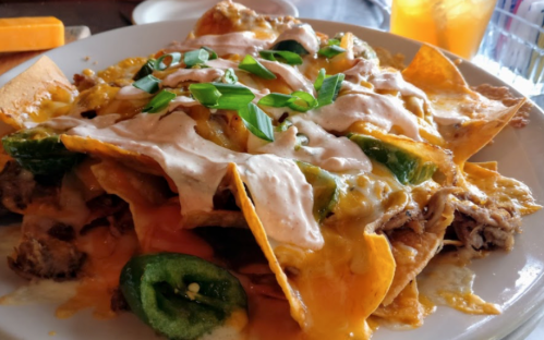 A plate of nachos topped with cheese, jalapeños, and a creamy sauce, garnished with green onions.