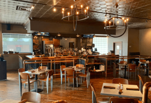 Interior of a restaurant featuring wooden tables, a bar area, and modern lighting fixtures.