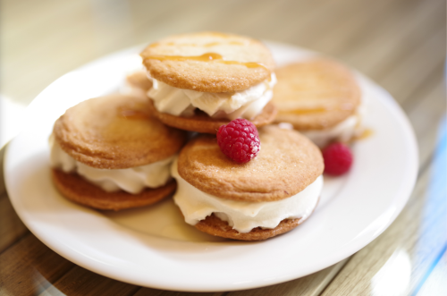 A plate of cream-filled cookies topped with a raspberry, arranged neatly on a wooden table.