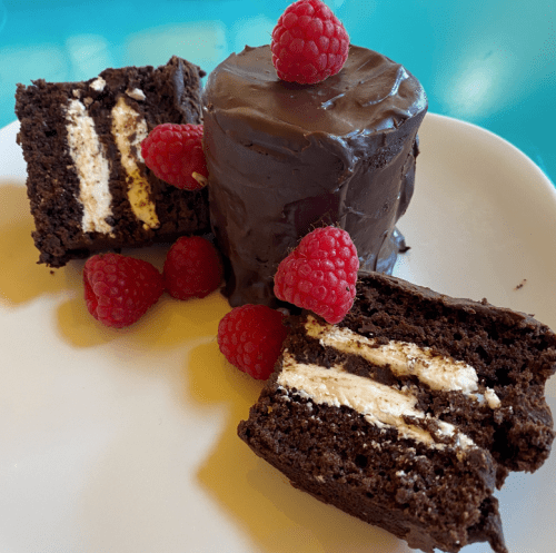 A plate with chocolate cake slices filled with cream, topped with raspberries and a chocolate-covered cake.
