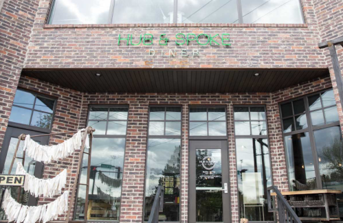 Exterior of Hub & Spoke Diner, featuring a brick facade and large windows, with an "OPEN" sign visible.
