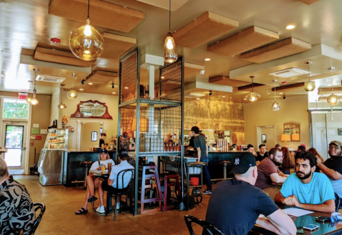 A busy café interior with patrons at tables, a counter in the background, and unique overhead decor.