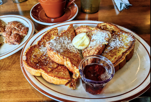 A plate of French toast topped with powdered sugar and a slice of butter, served with a small cup of syrup.
