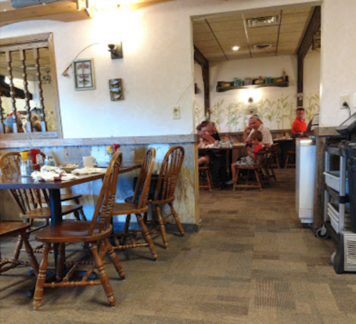 A cozy restaurant interior with wooden tables and chairs, featuring diners in the background and a warm atmosphere.