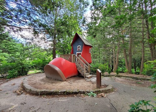 A whimsical red and blue house with a pointed roof, surrounded by trees and a small staircase leading to the entrance.