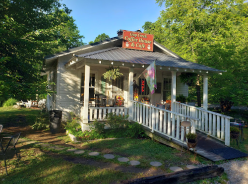 A charming coffee house with a porch, surrounded by greenery, featuring a sign that reads "Cup Creek Coffee House & Café."