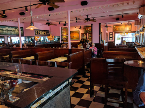 A cozy restaurant interior with pink walls, wooden booths, and checkered floors, filled with diners enjoying their meals.
