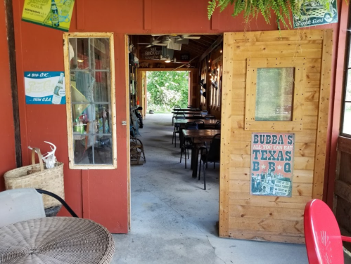 View of a rustic restaurant entrance with wooden doors, tables inside, and a sign for Bubba's BBQ.