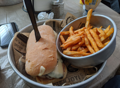 A sandwich with melted cheese and a knife in it, served with a side of crispy fries in a metal bowl.