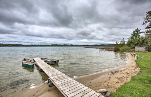 A wooden dock extends into a calm lake, with two boats moored nearby and overcast skies above.