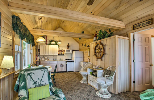 Cozy cabin interior with wooden walls, a kitchen area, and comfortable seating, featuring nautical decor and natural light.