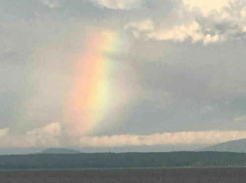 A soft rainbow appears in the sky above a landscape of clouds and distant mountains.