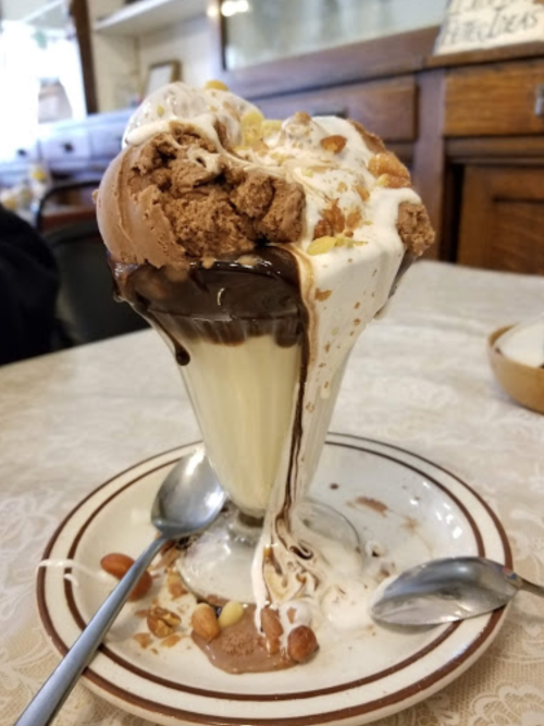A tall ice cream sundae with chocolate and vanilla ice cream, topped with whipped cream, chocolate sauce, and nuts.