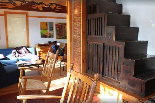 A cozy living room featuring wooden stairs with drawers, rocking chairs, and colorful artwork on the walls.