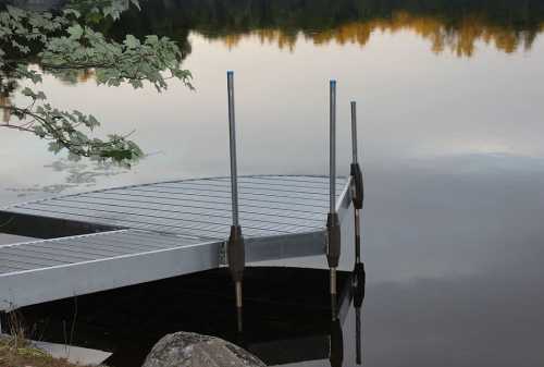 A metal dock extends into a calm lake, surrounded by trees reflecting in the water.