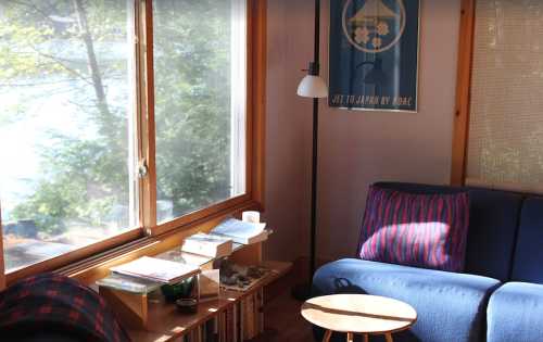 Cozy living room with a blue sofa, wooden table, and large window overlooking greenery. Bright and inviting atmosphere.