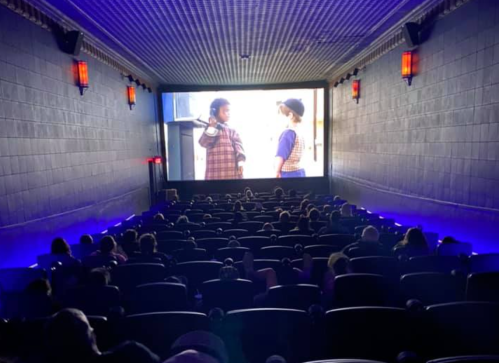A dimly lit movie theater with an audience watching a film on a large screen.