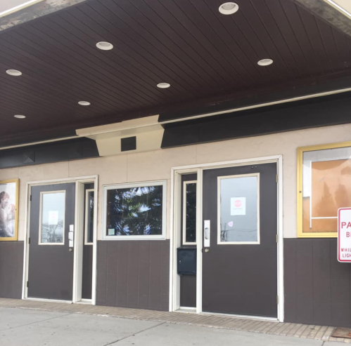 Exterior of a building featuring three doors, a dark overhang, and signs on the windows.
