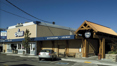 Exterior view of a restaurant and lounge with a wooden awning and a sign, featuring a clear blue sky.