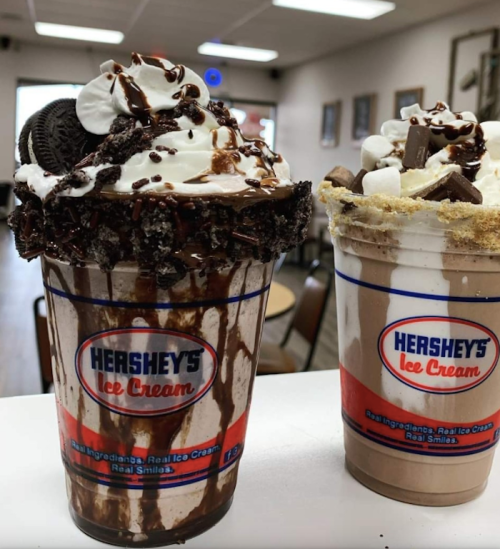 Two decadent ice cream shakes topped with whipped cream, chocolate syrup, and cookies, served in Hershey's cups.