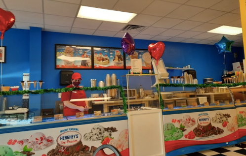 A brightly colored ice cream shop with a staff member serving ice cream, decorated with balloons and festive decor.