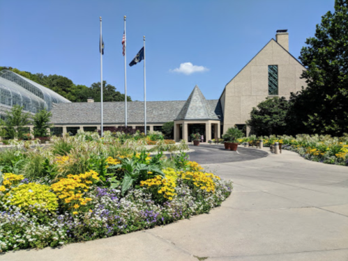 A landscaped entrance with colorful flowers, flags, and a modern building under a clear blue sky.