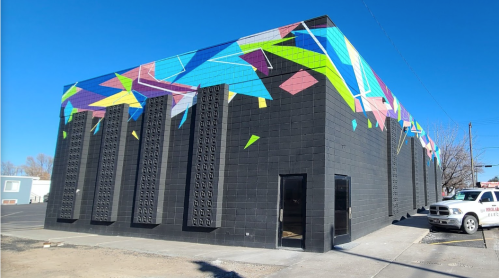 Colorful geometric mural on a black building exterior, featuring vibrant shapes against a clear blue sky.