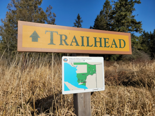 Signpost indicating a trailhead, featuring a directional arrow and a map of the surrounding nature preserve.