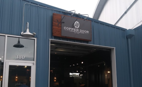 Sign for Copper Door Coffee Roasters on a blue building exterior.