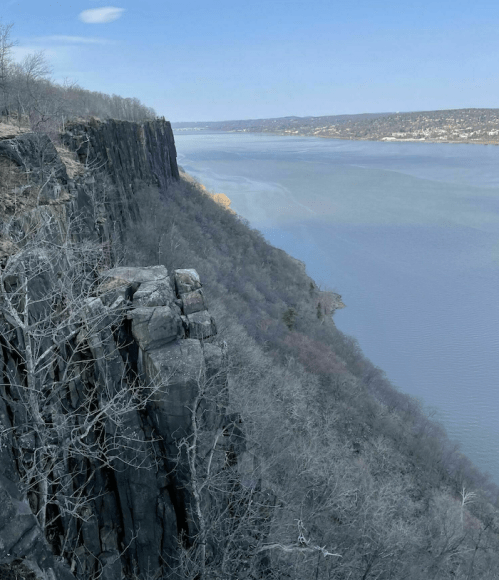 A scenic view of a river bordered by steep cliffs and bare trees under a clear blue sky.