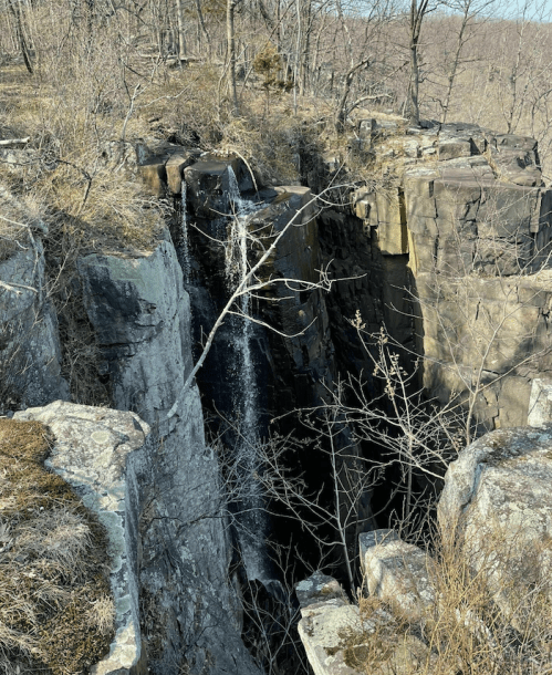 A waterfall cascading down a rocky cliff surrounded by bare trees and rugged terrain.