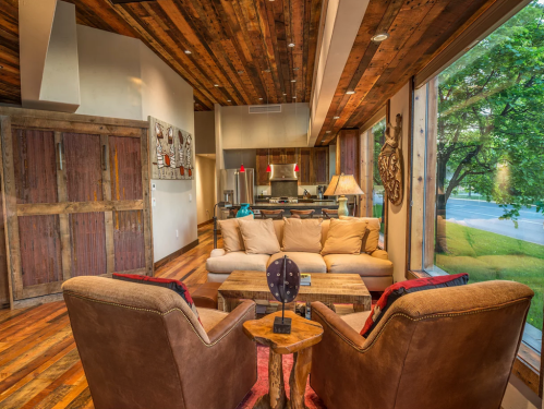 Cozy living room with wooden floors, a large window, and comfortable seating, featuring rustic decor and warm lighting.