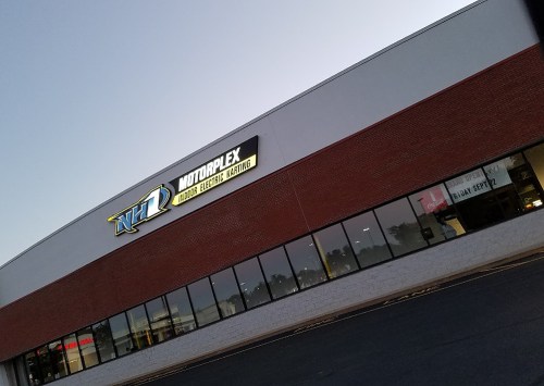 Exterior of a building with a sign that reads "Motorplex Indoor Racing Karting" at dusk.