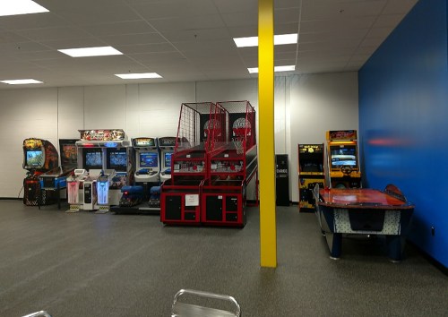 A game room featuring various arcade machines, including racing games, basketball hoops, and air hockey tables.