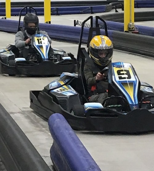 Two go-karts racing on a track, with drivers wearing helmets and focused on the race.