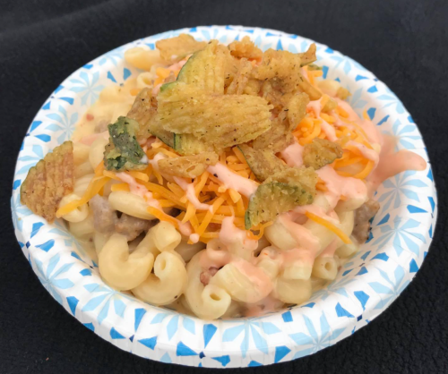 A bowl of macaroni and cheese topped with shredded cheese, sauce, and crispy fried zucchini chips.