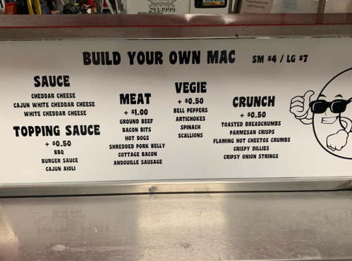Menu board for "Build Your Own Mac" with options for sauce, meat, veggies, and crunch toppings. Prices listed.