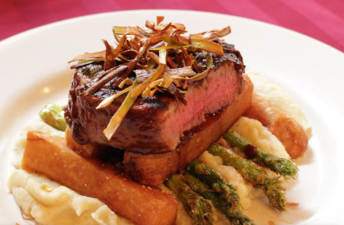 A beautifully plated steak topped with crispy leeks, served with asparagus and creamy mashed potatoes.