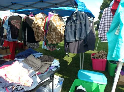 A vibrant outdoor market scene with clothing hanging on tents and a table stacked with various garments.