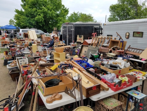 A bustling outdoor flea market filled with various antiques, collectibles, and household items on tables.