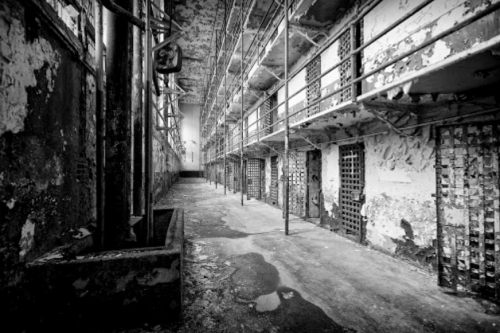 A dimly lit, abandoned prison corridor with peeling walls and empty cells.