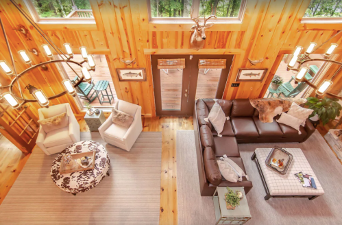 Cozy living room with wooden walls, modern furniture, and large windows overlooking a deck and greenery.