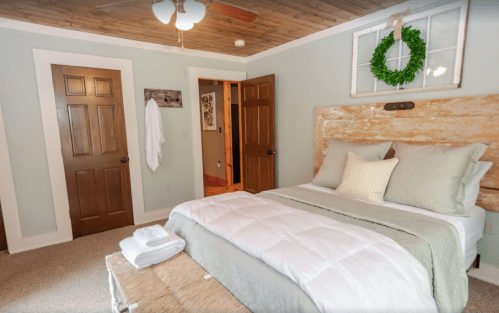 Cozy bedroom with a wooden headboard, green accents, and a wreath, featuring a bed, doors, and a warm atmosphere.
