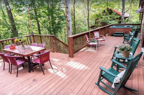 A spacious wooden deck surrounded by trees, featuring a dining table, chairs, and potted plants.